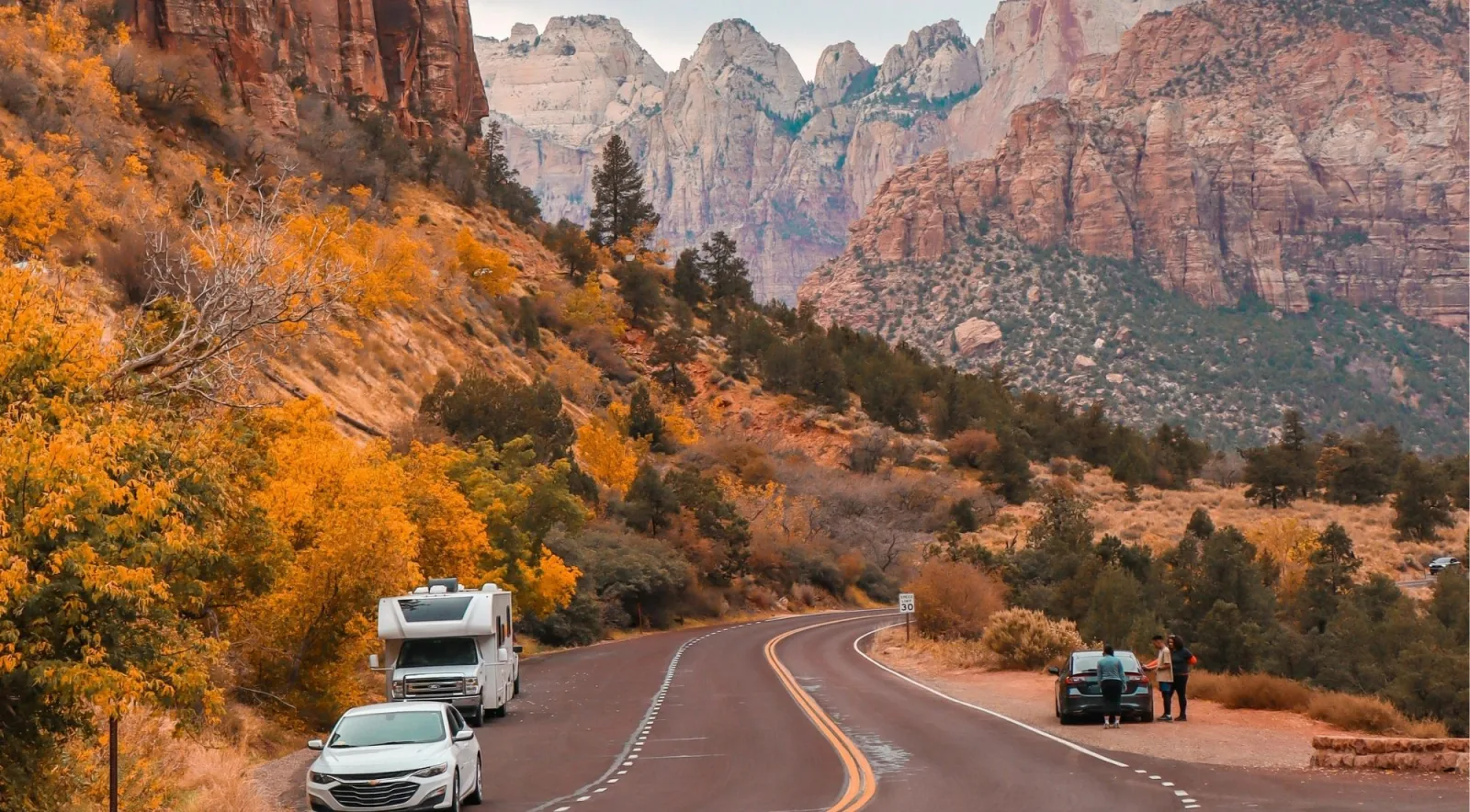 Vehicles pulled over on the Zion–Mount Carmel Highway beneath cliffs and autumn trees