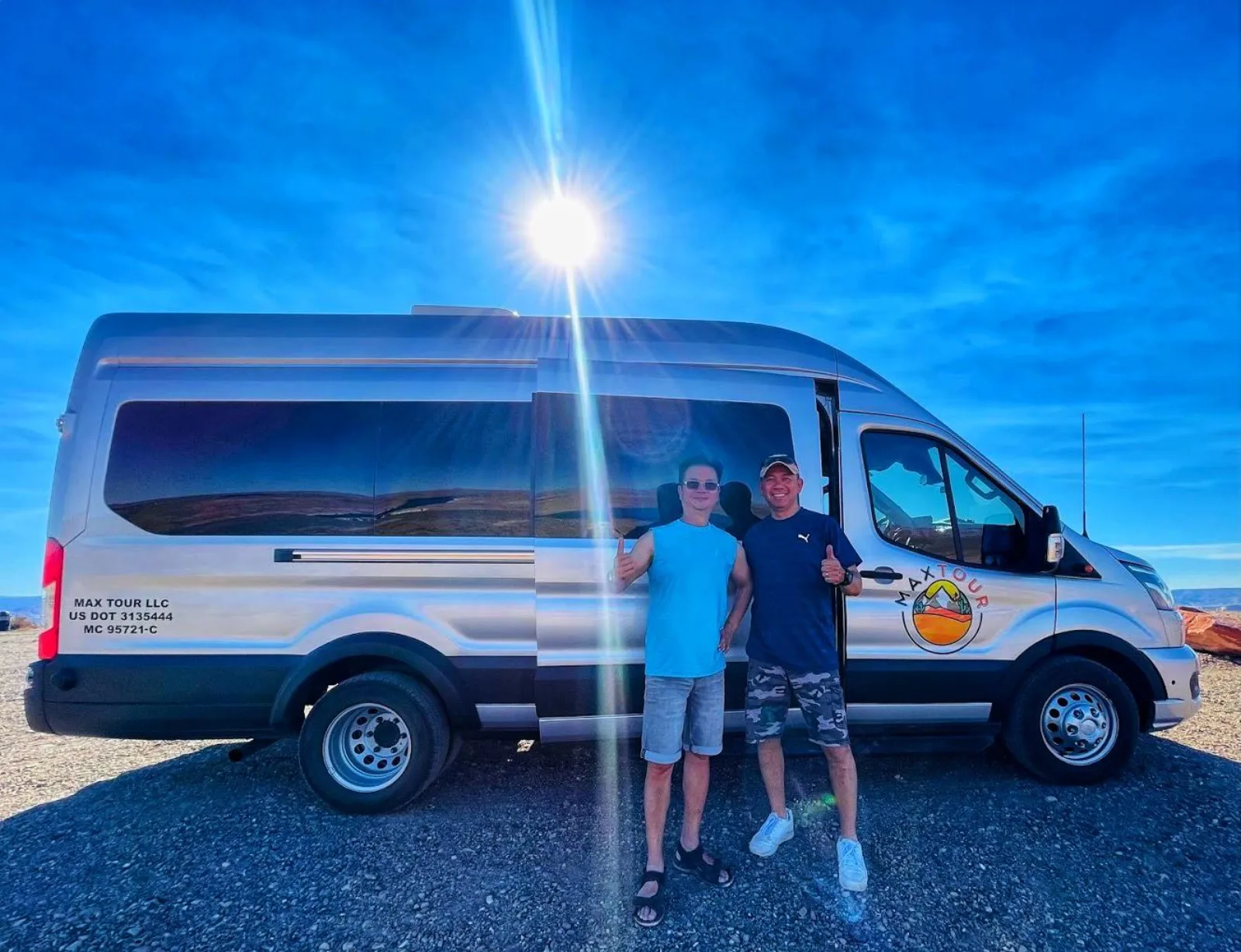 Two travellers beside the tour's white Mercedes van in bright desert sunshine