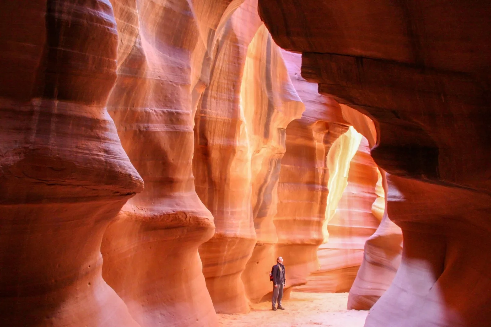 Lone figure standing in a beam of light inside a glowing slot canyon