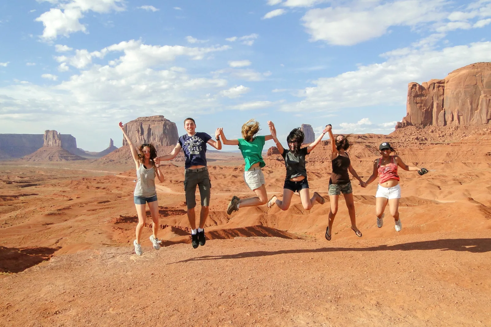 Tour group jumping in unison on the sand with the Monument Valley buttes behind them
