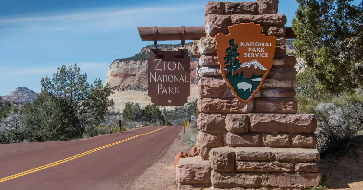 The stone Zion National Park entrance sign and National Park Service arrowhead beside the road into the park